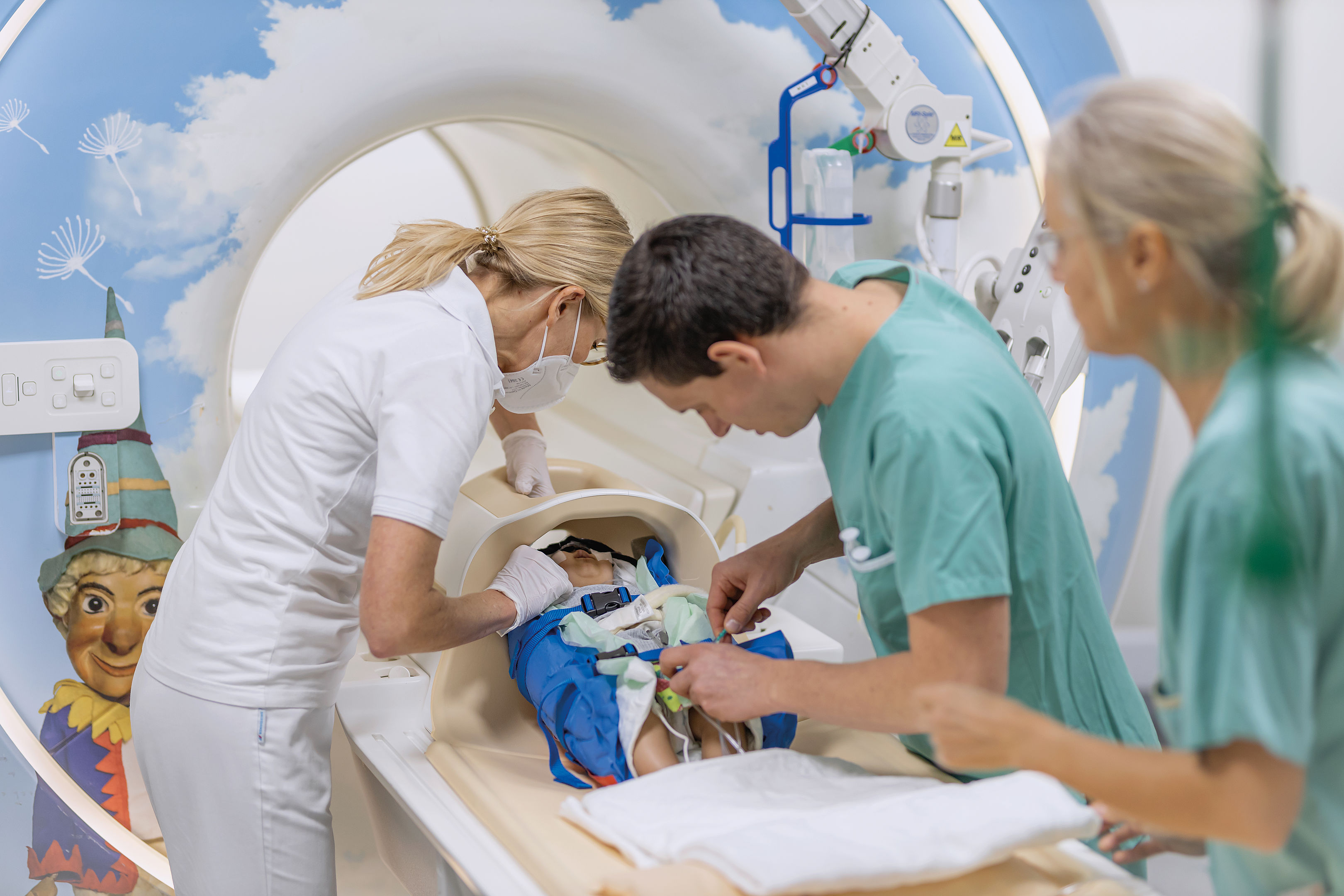Medizinisches Personal assistiert einem Kind in einem spielerisch gestalteten MRT-Raum und sorgt während des Verfahrens für Komfort und Sicherheit.