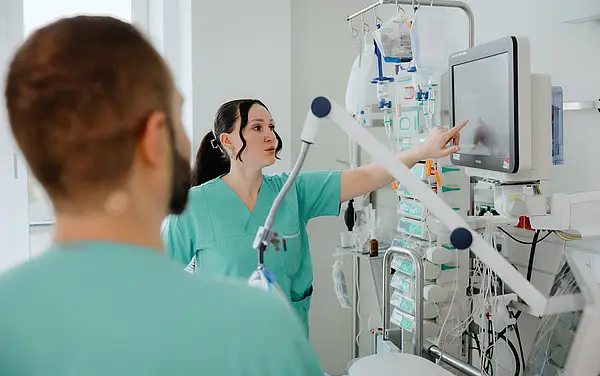 Eine Pflegekraft zeigt auf den Bildschirm eines medizinischen Geräts, während eine weitere Pflegekraft im Hintergrund zuschaut.