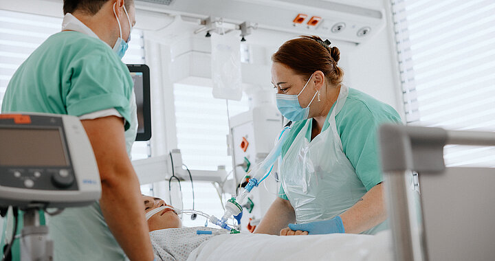 Zwei Intensivpflegekräfte stehen beim Patientenbett zusammen.