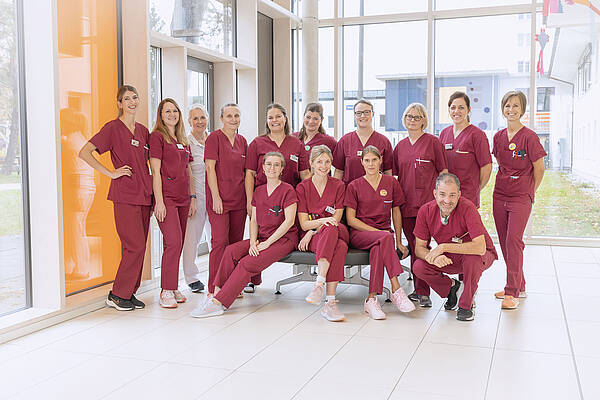 Eine Gruppe von medizinischem Fachpersonal in roten Uniformen posiert gemeinsam in einem hellen, modernen Flur.