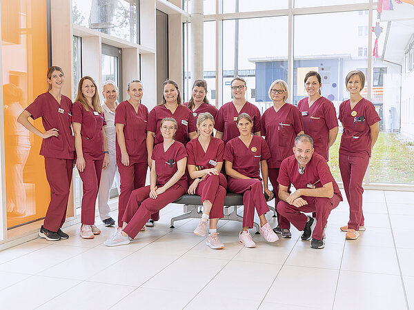 Eine Gruppe von medizinischem Fachpersonal in roten Uniformen posiert gemeinsam in einem hellen, modernen Flur.