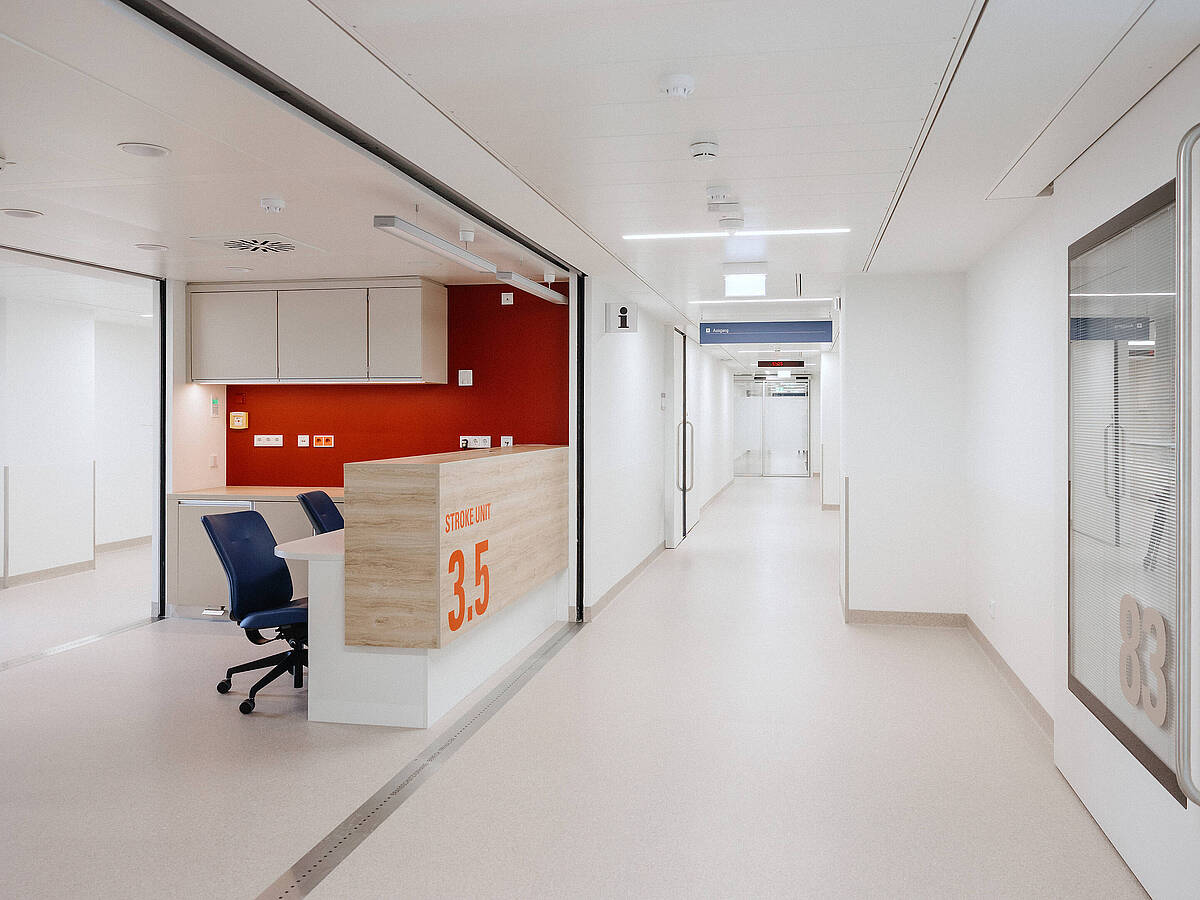 Blick auf einen modernen Krankenhausflur mit einem Empfangstresen und einem leeren Bürostuhl. Der Flur ist hell und minimalistisch gestaltet.