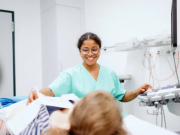 Pflegekraft spricht lächelnd mit einer Patientin im Krankenhauszimmer.
