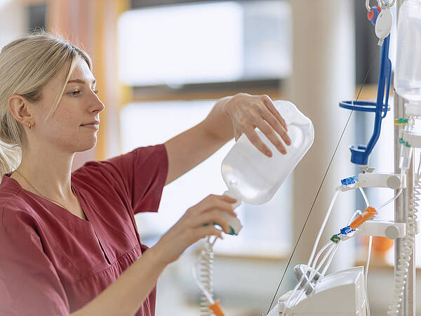 Ein Mitarbeiter des Gesundheitswesens in einer kastanienbraunen Uniform legt in einem Krankenhaus eine Infusion an.