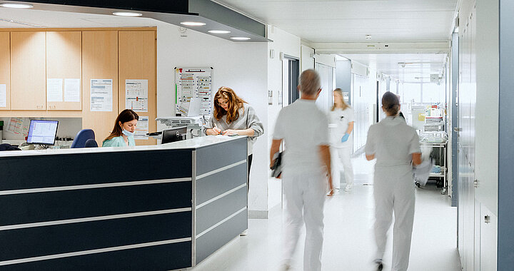 Zwei Pflegekräfte gehen durch einen hellen Krankenhausflur.