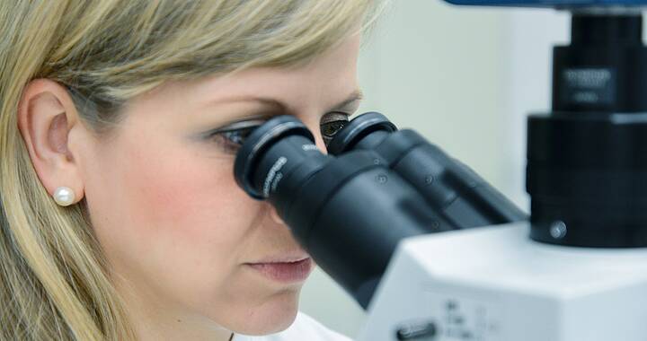 Eine blonde Frau in weiße Kittel sieht durch ein Mikroskop. 