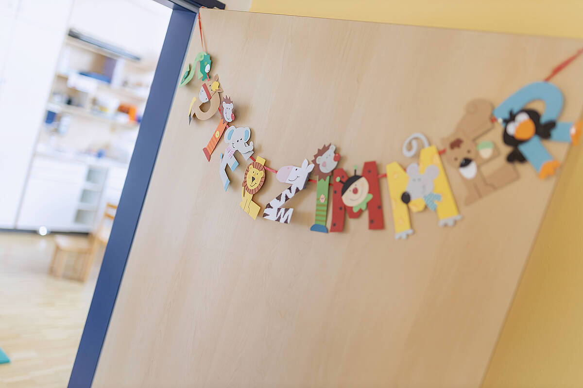 Farbenfrohe Dekorationen mit Tiermotiven hängen an einem Holzbrett in einem hellen, gemütlichen Raum.