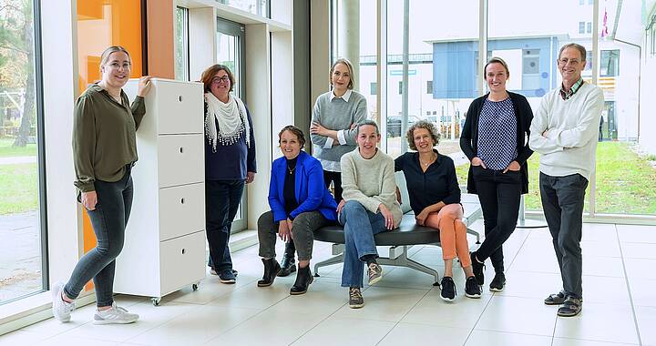 Acht Pflegerinnen und Pfleger des schwäbischen Kinderkrebszentrums stehen im Foyer und lächeln in die Kamera.