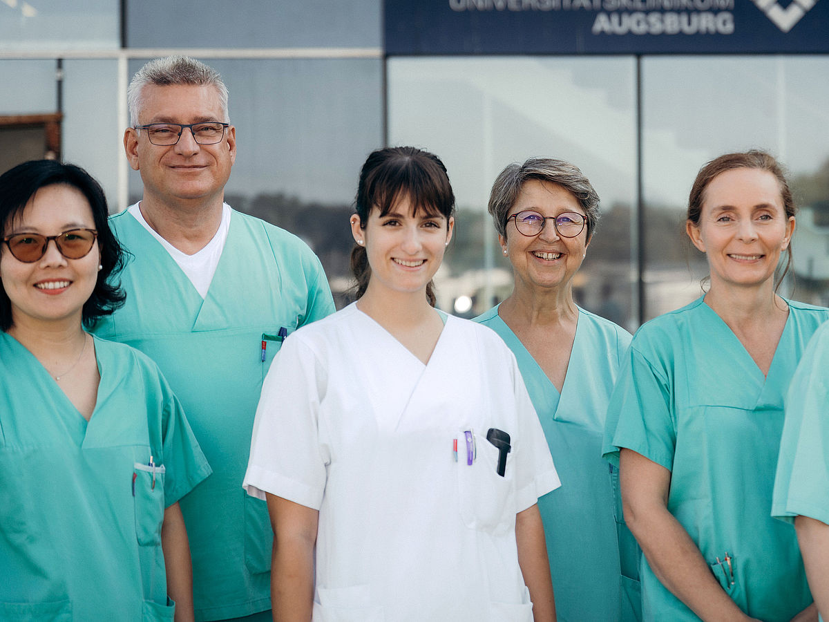 Medizinisches Team des Zentrums für Intensivtherapie des Universitätsklinikums Augsburg steht vor dem Gebäude für ein Gruppenfoto.