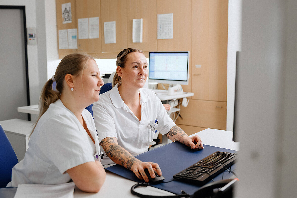 Zwei Mitarbeiterinnen aus der Pflege arbeiten gemeinsam an einem Computerarbeitsplatz im Krankenhaus.