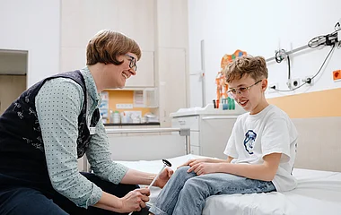 Betreuung von Kindern im Krankenhaus Mitarbeiterin spricht mit einem Kind auf einem Krankenhausbett.