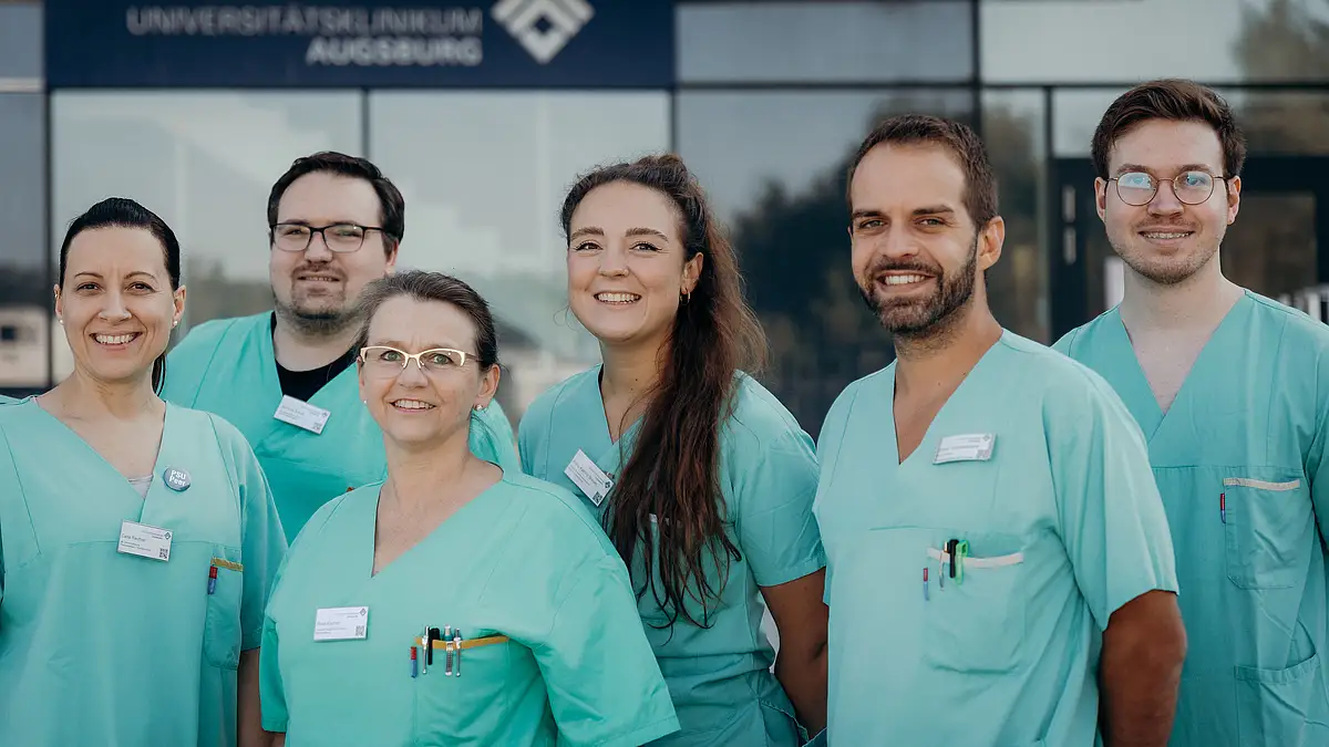 Gruppe von medizinischen Fachkräften in grünen Klinik-Kitteln vor einem Klinikgebäude.